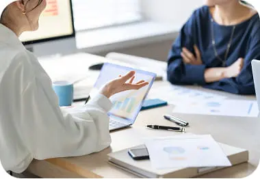 ノートパソコンと資料を使いながら会議を行う2人のビジネスシーン、手振りで説明する様子