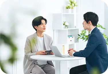 丸テーブルでノートパソコンを前に向かい合って会話する2人の男性、打ち合わせ風景