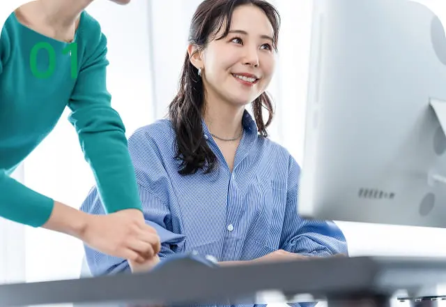 パソコン画面を見ながら笑顔で会話をしている2人のビジネスパーソン