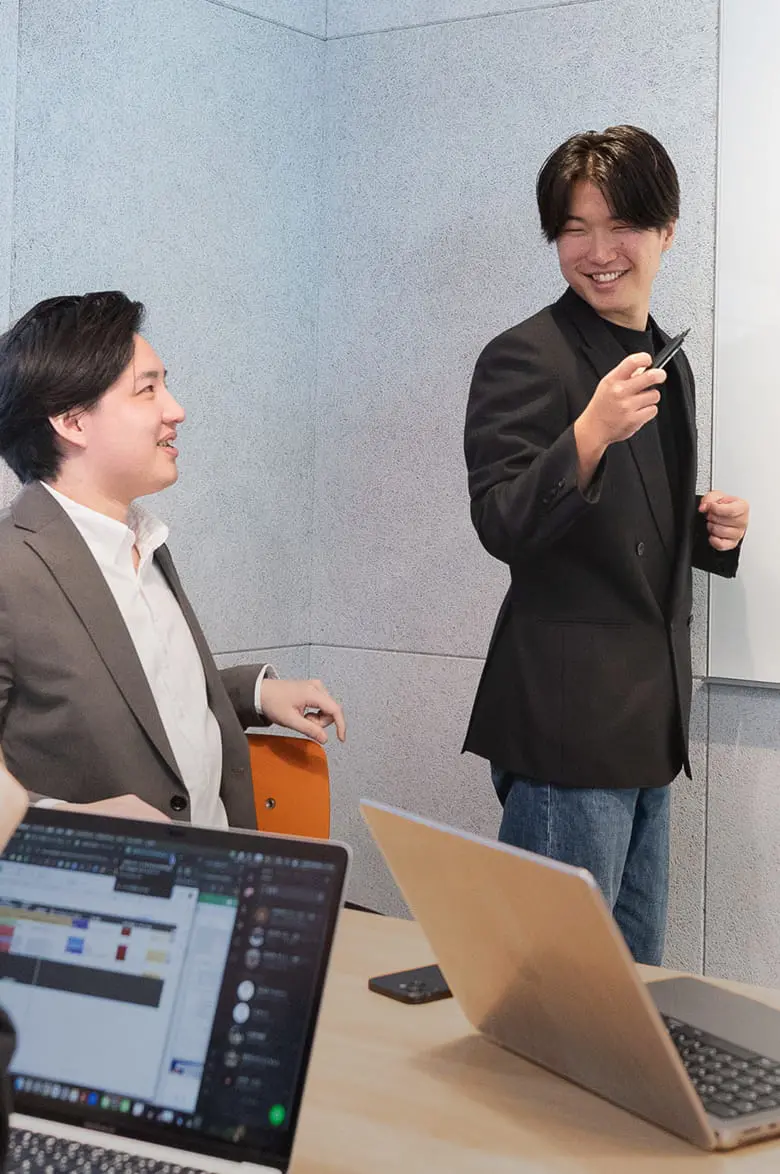 会議室で3人のビジネスパーソンがパソコンを囲んで会話をしている様子