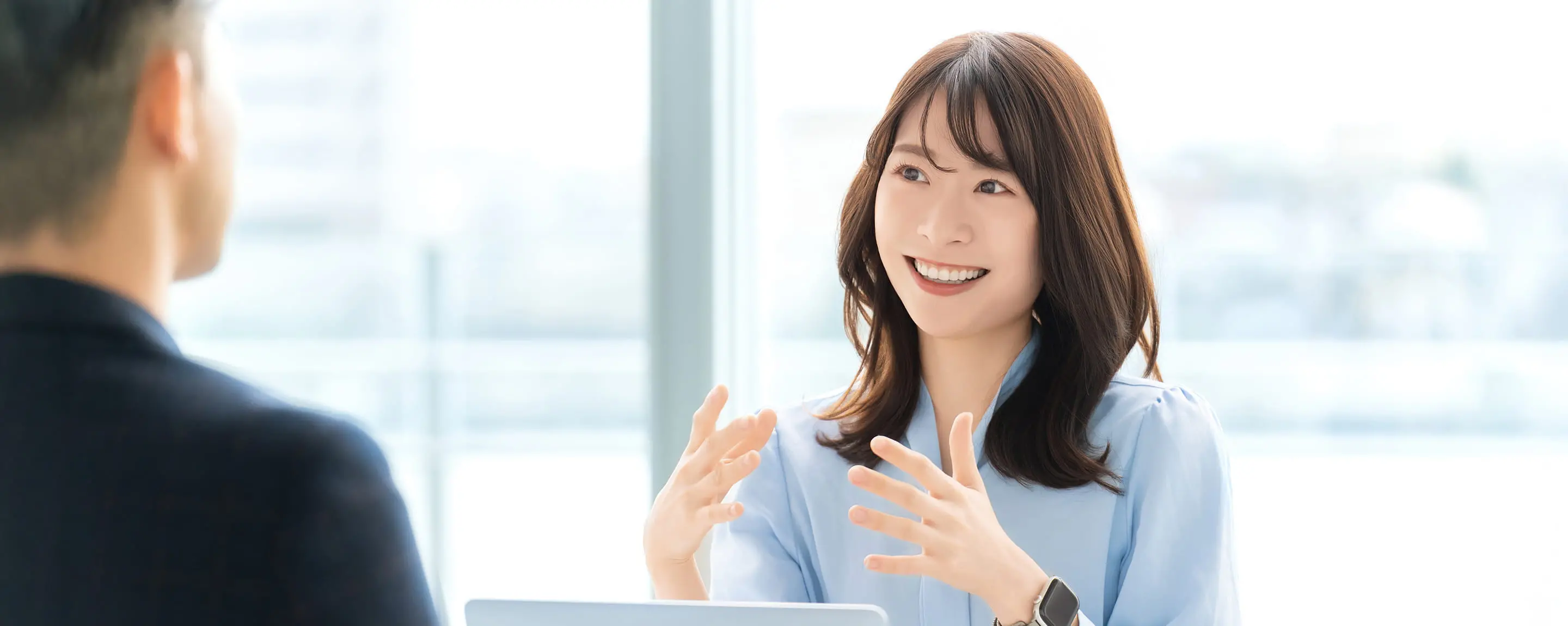 笑顔の女性が明るいオフィスで対面の男性と会話をしているビジネスシーン